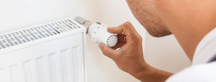 Handwerker prüft Thermostat-Regler am Heizkoerper
